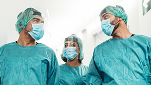 Three medical professionals in scrubs, hair coverings and masks