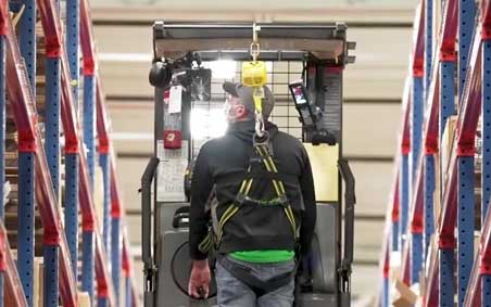 A warehouse worker wearing PPE including fall protection and a hard-hat.