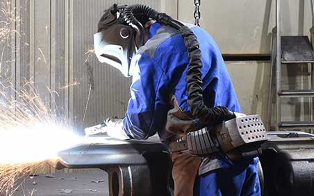 Worker grinding a weld wearing S.C.B.A and welding PPE in an enclosed environment.