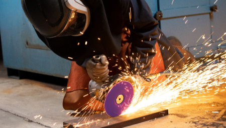 A worker using a purple 3M Cubitron abrasive disck with sparks.