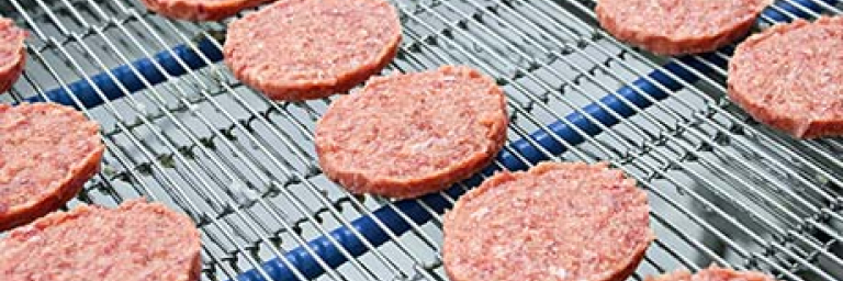 Multiple rows of meat patties on a food production line.