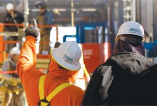 Set in an industrial warehouse, plant or facility, two men walk through the facility (with backs turned to camera) wearing personal protective equipment (PPE): Airgas branded hardhats.