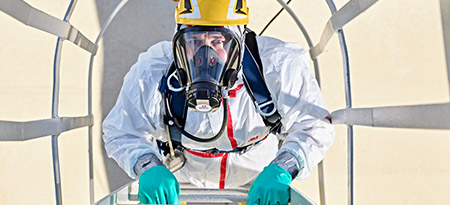 An industrial worker in head-to-toe PPE breathes safely by wearing a 3M Scott full-face air-purifying respirator.