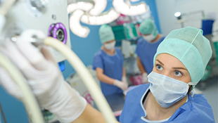 A nurse with hair and face coverings operates a medical gas machine.