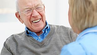 An old man wearing a gray sweater laughing.