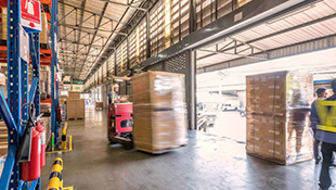 A blurry pallet of boxes on a lift moves through a warehouse.