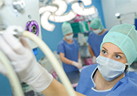 A nurse with hair and face coverings operates a medical gas machine.