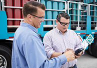 An Airgas driver delivering cylinders to a customer who is signing a digital proof of receipt (POD) on a handheld device.