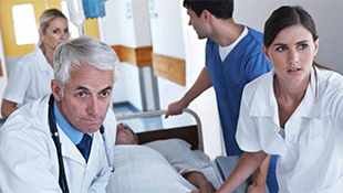 A medical team pushes a patient's bed through the hall