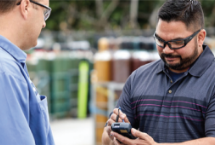 An Airgas driver delivering cylinders to a customer who is signing a digital proof of delivery (POD) on a handheld device.