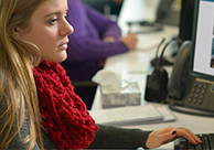 A blond woman in a red scarf, working in an office bullpen