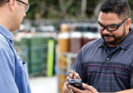 An Airgas driver delivering cylinders to a customer who is signing a digital proof of receipt (POD) on a handheld device.