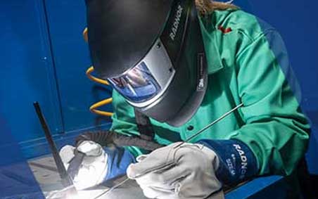 Welder using RADNOR welding tools and consumables, while wearing RADNOR welding helmet by 3M Speedglas, welding jacket and welding gloves.