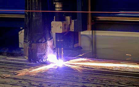 A worker in full PPE plasma cutting sheet metal