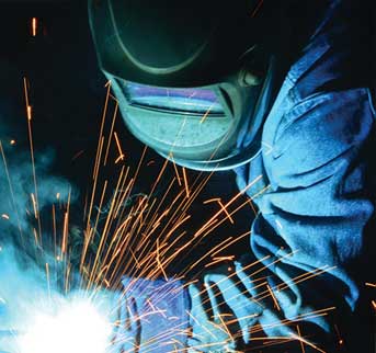 A MIG welder in a RADNOR helmet behind a small shower of sparks