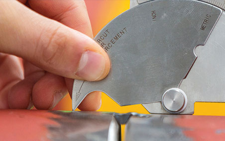 Welder using a fillet gauge to measure a weld.