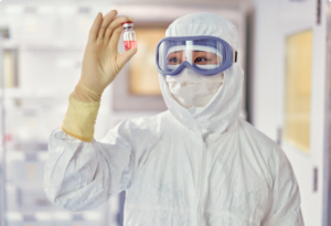 Worker in lab wearing white DuPont protective gear is holding a small tube of pink liquid.