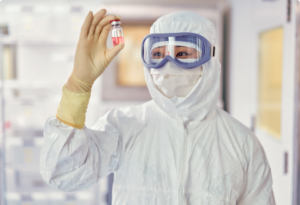 Press to view Worker in lab wearing white DuPont protective gear is holding a small tube of pink liquid.