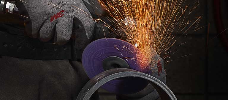 Sparks fly from a grinding machine operated by a worker in protective face gear..