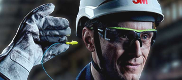A worker with protective 3M eye and head gear and gloves places an earplug into his ear.