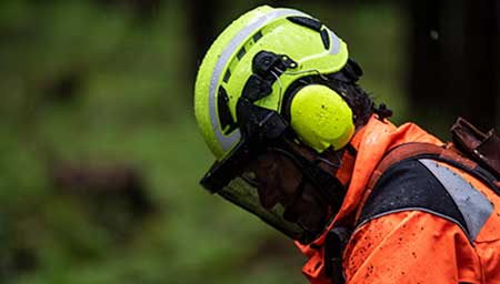 A worker with protective ear, face and head gear looks down at the job.