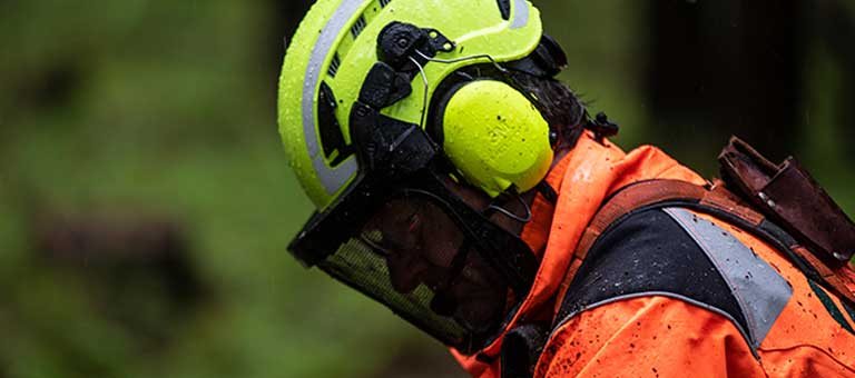 A worker with protective ear, face and head gear looks down at the job.