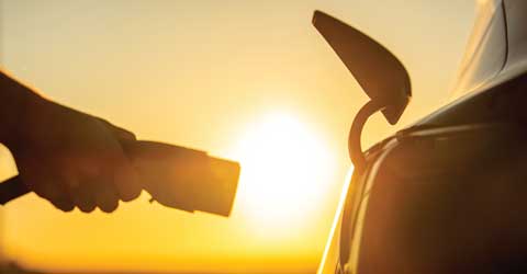 Plugging in an electric vehicle at sunset