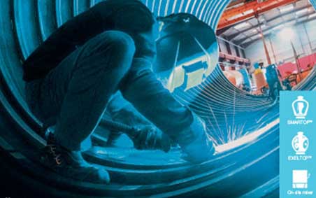 Welder standing inside of a large corrugated metal pipe performing a weld on the interior of the pipe underneath.