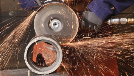 Sparks fly from a grinding machine operated by a worker in 3M protective face gear.