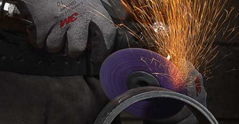 Sparks fly from a grinder operated by a worker in 3M protective gear.