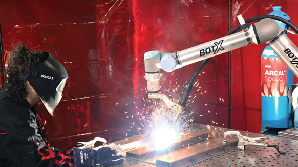 A welder wearing a RADNOR welding helmet operating a Bot-X welding machine.