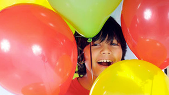 A child peeking through a bunch of red and yellow helium baloons