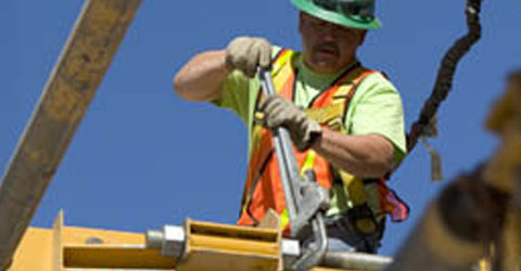 A construction worker in PPE with a giant wrench turning a bolt on a large piece of construction equipment