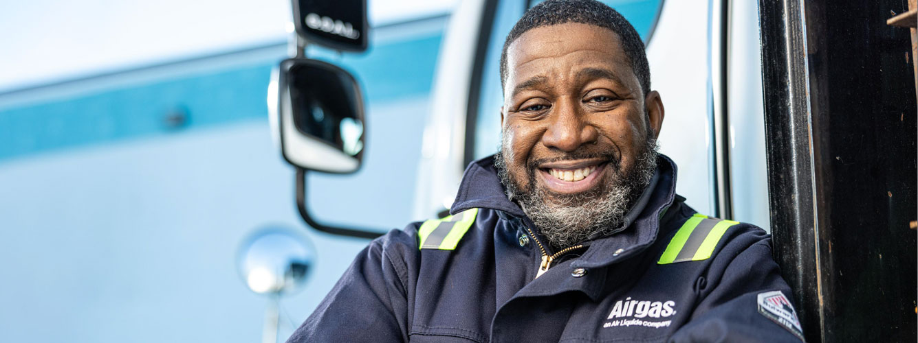 Airgas CDL truck driver stands in front of the truck smiling.