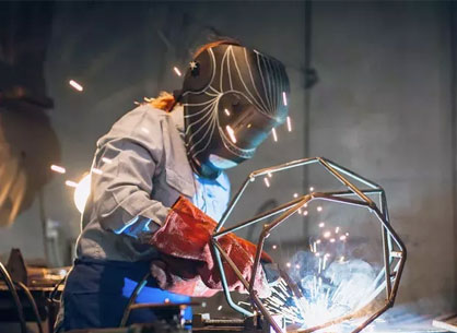A woman welding and wearing proper PPE.