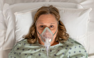A woman in a hospital bed wearing an oxygen mask
