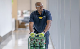 A hospital worker pushing a cart of portable oxygen tanks down a hallway