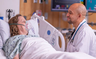 A doctor sitting next to a bed speaking with an elderly patient