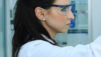 A woman scientist wearing safety glasses and a lab coat.