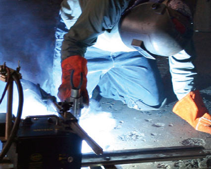 Welder wearing welding helmet on knees flux cored arc welding (FCAW) stainless steel using ARCAL Flux premium shielding gas.