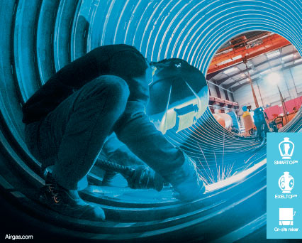 Welder standing inside of a large corrugated metal pipe performing a weld on the interior of the pipe underneath.