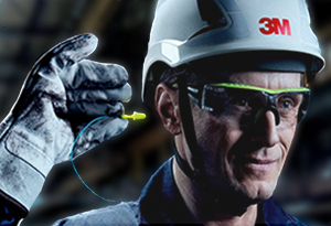 A worker with protective 3M eye and head gear and gloves places an earplug into his ear.
