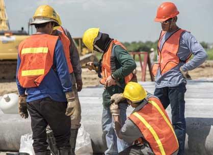 Five construction workers stand on a jobsite wearing personal protective equipment - PPE
