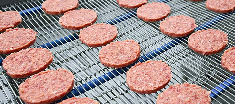 Frozen meat patties on a food production line; with title in upper left corner: Freezing and Chilling Food.
