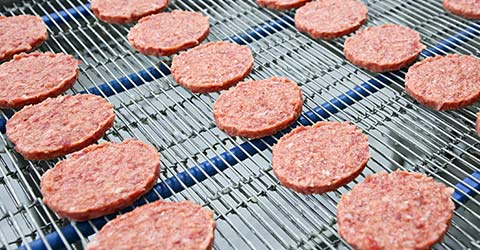 Rows of raw hamburger patties on a conveyor belt
