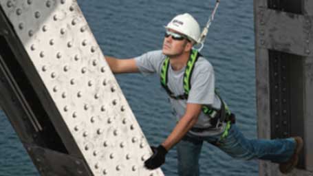 A worker wearing a Honeywell Miller fall-protection harness scales a beam.