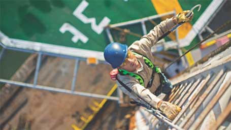 From a top-down view, a worker wearing a Honeywell Miller harness climbs a ladder.