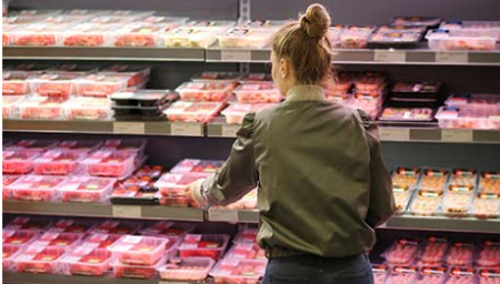 Shopper selecting packaged meat from a refrigerated supermarket display.