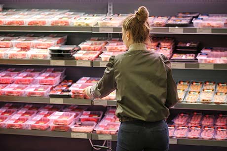 Shopper selecting packaged meat from a refrigerated supermarket display.