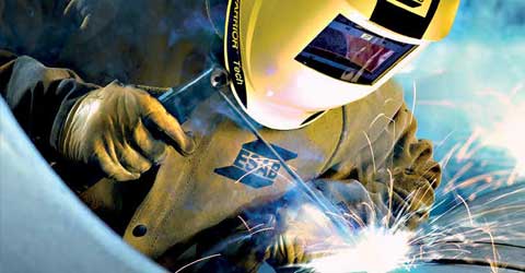 A welder performs a stick-welding application while wearing ESAB branded welding safety clothing and personal protective equipment (PPE), including a welding helmet, welding gloves and a welding jacket.